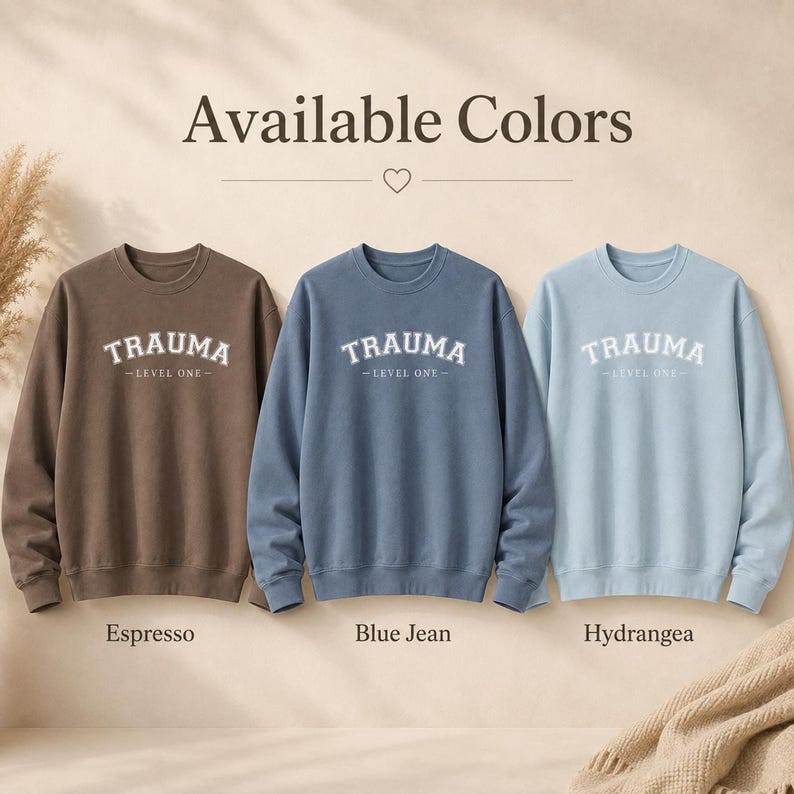 Three crewneck sweatshirts in Espresso, Blue Jean, and Hydrangea with the TRAUMA LEVEL ONE text.