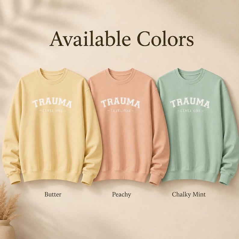 Three crewneck sweatshirts in Butter, Peachy, and Chalky Mint, all with the TRAUMA LEVEL ONE design.