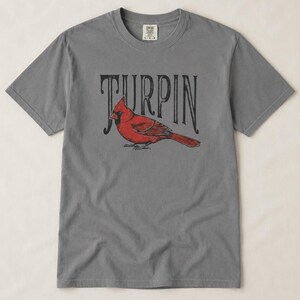 A slate gray short-sleeve t-shirt featuring a red cardinal and black vintage Turpin text centered on the chest.