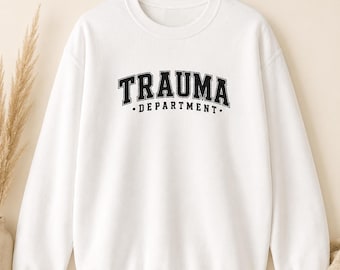 Puede incluir: Una sudadera blanca de manga larga con el texto negro TRAUMA DEPARTMENT impreso en una fuente universitaria en el pecho. La prenda incluye el texto Trauma Department Sweatshirt y Gildan 18000 Embroidered Look en la parte superior.