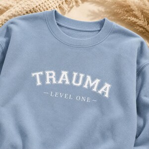 Close-up of the light blue sweatshirt fabric showing the white TRAUMA LEVEL ONE lettering.