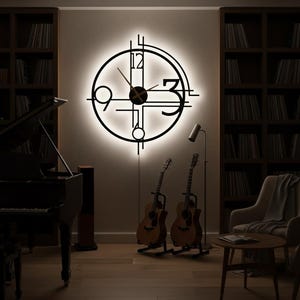 May include: A modern, black metal wall clock with a circular design and illuminated background. The clock features a minimalist style with the numbers 3, 9, and 12 clearly visible. The room also includes a piano, guitars, and bookshelves.