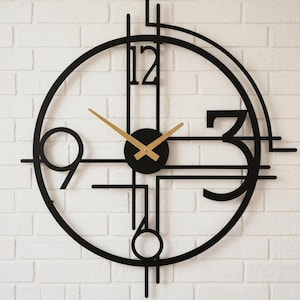 Può includere: Un moderno orologio da parete in metallo nero con lancette dorate e un quadrante nero. L'orologio presenta i numeri 12, 3, 6 e 9, con un design minimalista. È montato su un muro di mattoni bianchi.