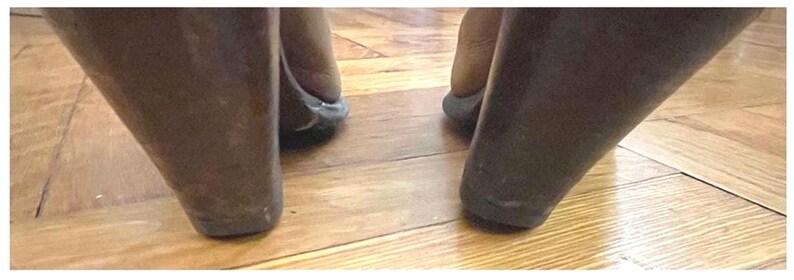May include: A pair of dark brown wedge heels featuring a smooth, solid-colored exterior. The shoes have a thick, tapered wedge heel design that provides a stable base, with the back of the heel clearly visible as it rests on a wooden floor surface.