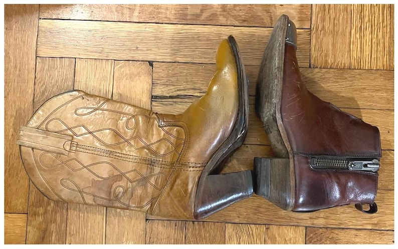 May include: A pair of leather boots consisting of one tall tan western-style boot with decorative stitching and a stacked heel, and one shorter dark brown ankle boot featuring a side zipper closure, a pointed toe, and a metallic toe cap detail.