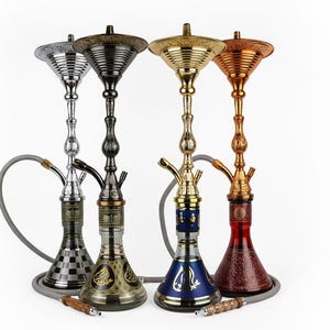 Puede incluir: Cuatro narguiles ornamentados en plata, negro, dorado y cobre. Cada narguile tiene una base, un tallo y un cuenco decorativos, con una manguera y una boquilla. Los narguiles están dispuestos sobre un fondo blanco.