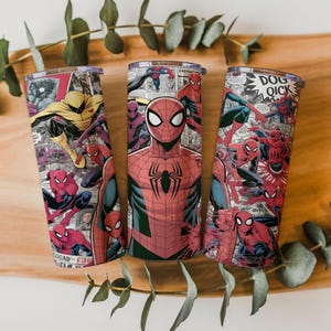 K&ouml;nnte beinhalten: Drei Edelstahlbecher mit Spider-Man-Comic-Motiven. Die Designs zeigen Spider-Man in verschiedenen Posen, mit Comic-Panels und Text. Die Becher haben transparente Deckel und sind auf einem Holzuntergrund platziert.
