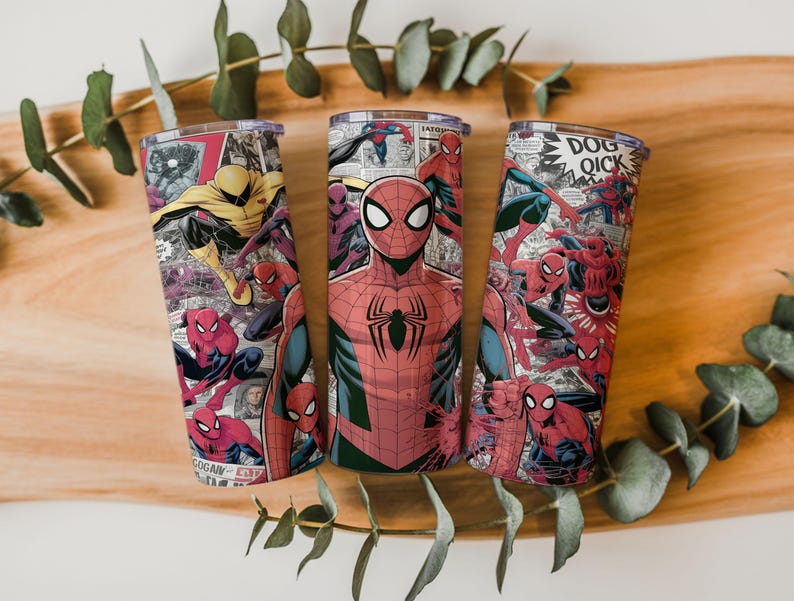 K&ouml;nnte beinhalten: Drei Edelstahlbecher mit Spider-Man-Comic-Motiven. Die Designs zeigen Spider-Man in verschiedenen Posen, mit Comic-Panels und Text. Die Becher haben transparente Deckel und sind auf einem Holzuntergrund platziert.