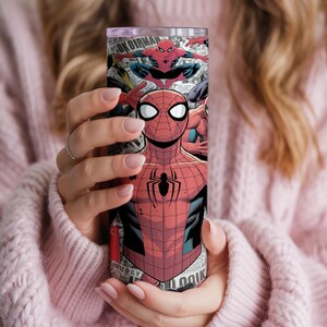 K&ouml;nnte beinhalten: Ein hoher, zylindrischer Becher mit einem Comic-Design von Spider-Man. Der Becher ist haupts&auml;chlich rot und schwarz, mit wei&szlig;en Akzenten und einem schwarzen Spinnenemblem. Der Hintergrund enth&auml;lt Comic-Panels und Text.