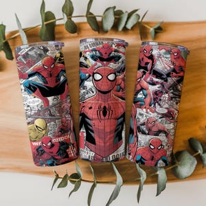 K&ouml;nnte beinhalten: Drei Edelstahlbecher mit einem Spider-Man-Comic-Design. Die Becher sind zylindrisch, mit einem transparenten Deckel und einem umlaufenden Aufdruck von Spider-Man in verschiedenen Actionposen, vor dem Hintergrund von Comic-Panels. Das Farbschema ist haupts&auml;chlich rot, blau und schwarz.