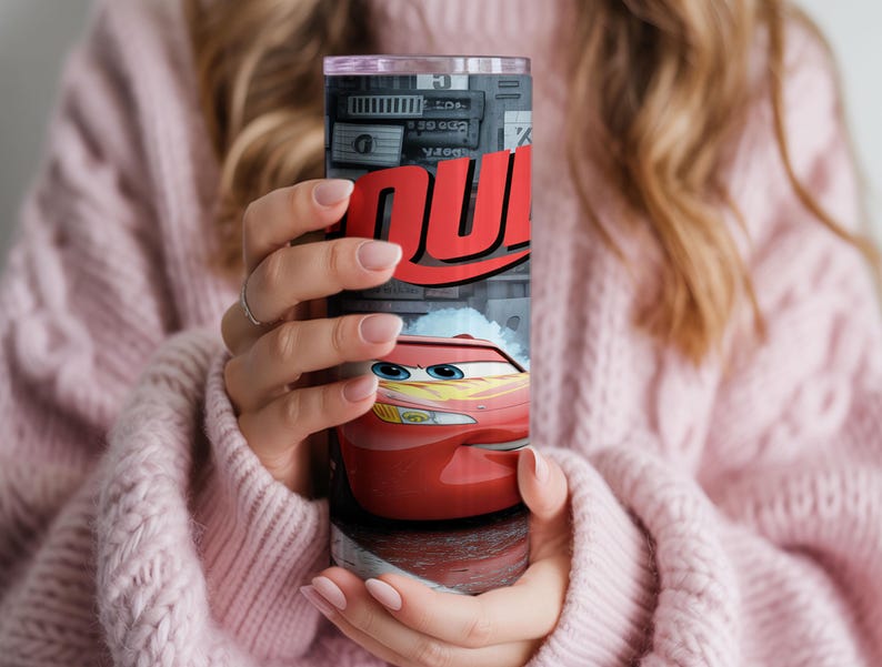 Pu&ograve; includere: Un bicchiere cilindrico in acciaio inossidabile con una stampa grafica di un'auto da corsa rossa con occhi blu e decalcomanie a forma di fulmine giallo. Il design include il testo rosso in grassetto "QU" su sfondo grigio con dettagli.