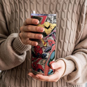 K&ouml;nnte beinhalten: Ein hoher, isolierter Becher mit einem Comic-Design mit Spider-Man und anderen Charakteren. Der Becher hat einen schwarzen Deckel und einen wei&szlig;en Strohhalm. Das Design umfasst rote, blaue, gelbe und schwarze Farben.