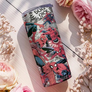 K&ouml;nnte beinhalten: Ein Edelstahlbecher mit Comic-Design, der Spider-Man-Illustrationen in Rot, Blau und Schwarz zeigt. Der Becher hat einen transparenten Deckel. Er ist von rosa Rosen und wei&szlig;en Blumen umgeben.