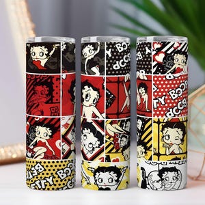 May include: Three stainless steel tumblers featuring a Betty Boop design. Each tumbler has a different color scheme, including red, black, and yellow, with a repeating pattern of Betty Boop images and text. The tumblers are cylindrical and appear to be insulated.