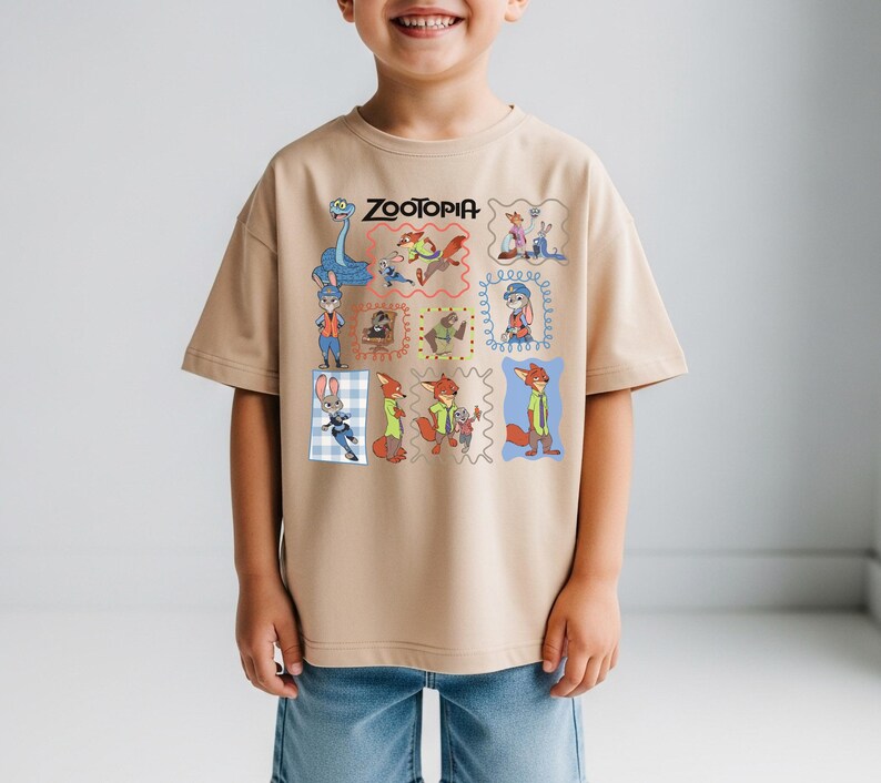 May include: Tan t-shirt featuring the word "ZOOTOPIA" above a grid of cartoon character illustrations. The shirt has short sleeves and is worn by a child. The illustrations include a snake, a bunny, and a fox.