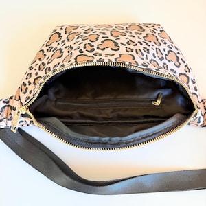 K&ouml;nnte beinhalten: Rosa Bauchtasche mit Leopardenmuster. Die Tasche hat ein schwarzes Innenfutter und einen goldenen Rei&szlig;verschluss. Ein schwarzer Gurt ist am Beutel befestigt.