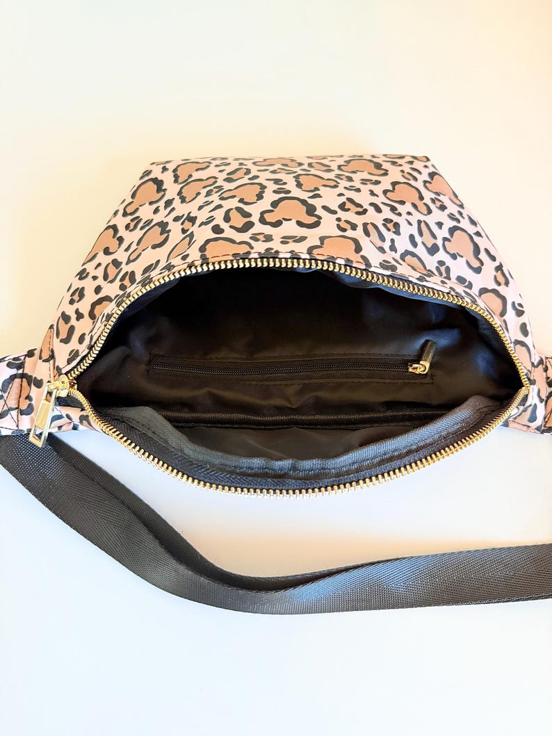 K&ouml;nnte beinhalten: Rosa Bauchtasche mit Leopardenmuster. Die Tasche hat ein schwarzes Innenfutter und einen goldenen Rei&szlig;verschluss. Ein schwarzer Gurt ist am Beutel befestigt.