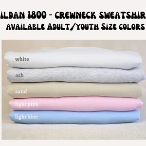 A stack of five different colored crew neck sweatshirts, with each color labeled: white, ash, sand, light pink, and light blue.