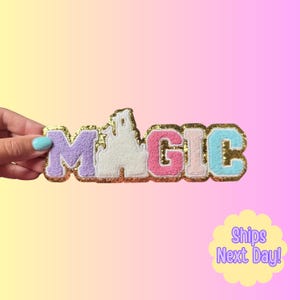 May include: A chenille patch featuring the word MAGIC with a castle silhouette replacing the letter A. The letters are in pastel purple, white, pink, peach, and light blue, all outlined with a thick, shimmering gold glitter border.