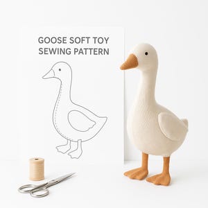 May include: A plush, cream-colored goose toy with a brown beak and feet stands next to a paper with a goose sewing pattern. The paper also has the text "GOOSE SOFT TOY SEWING PATTERN". A spool of thread and scissors are also in the image.