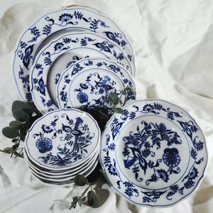 May include: A collection of white porcelain plates with a blue floral design. The set includes various sizes of plates, from large dinner plates to small saucers. The blue and white pattern is intricate and detailed, with a scalloped edge.