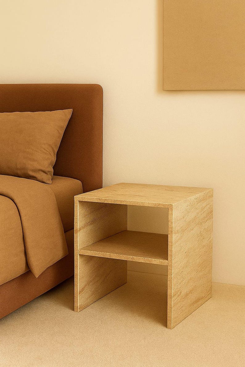 May include: A light-colored wooden nightstand with two shelves. The nightstand is next to a bed with a brown headboard and bedding. The room has a neutral color palette.