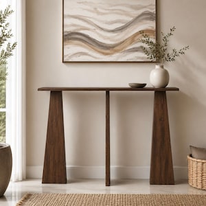 May include: A dark brown wooden console table featuring a long, flat rectangular top supported by three vertical, tapered legs. The table has a smooth, polished finish and a clean, linear structure, providing a stable surface for display.