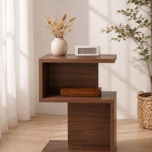 May include: A modern, dark brown wooden side table with a unique, open design. The table features a top shelf with a small white clock displaying 7:15 and a vase with dried flowers. A wooden box sits on the middle shelf.