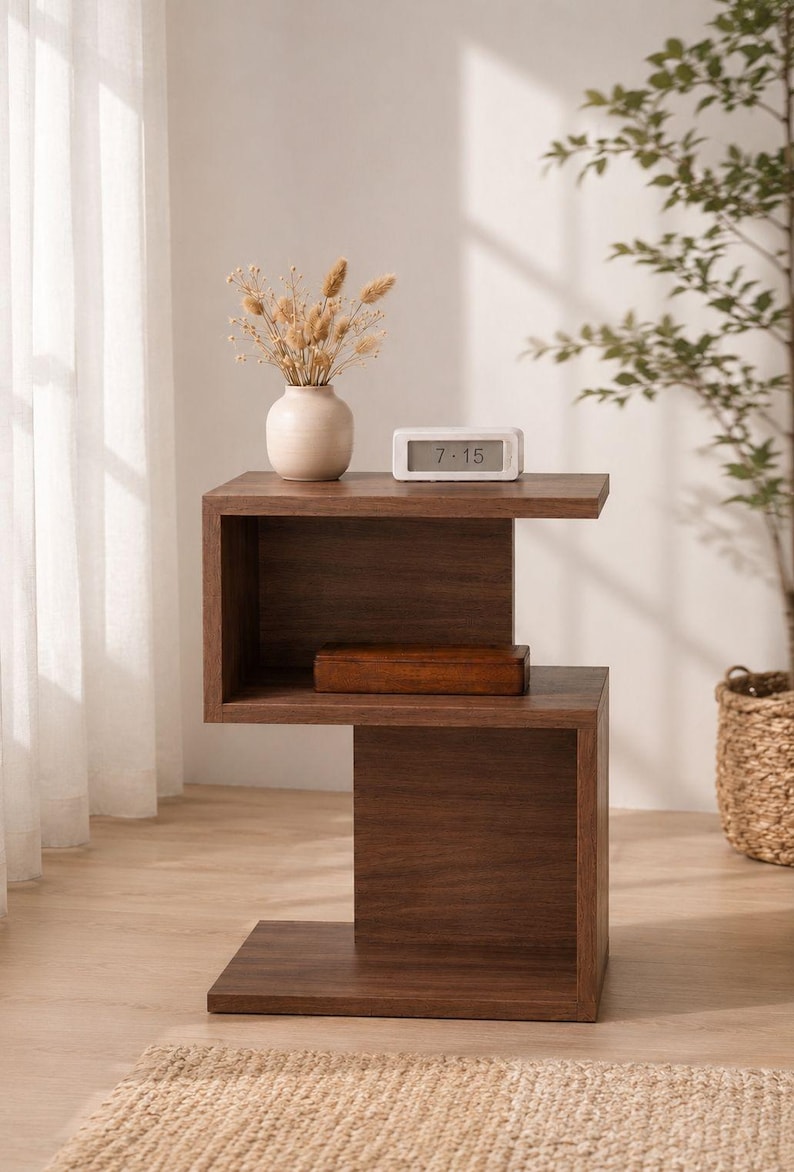 May include: A modern, dark brown wooden side table with a unique, open design. The table features a top shelf with a small white clock displaying 7:15 and a vase with dried flowers. A wooden box sits on the middle shelf.