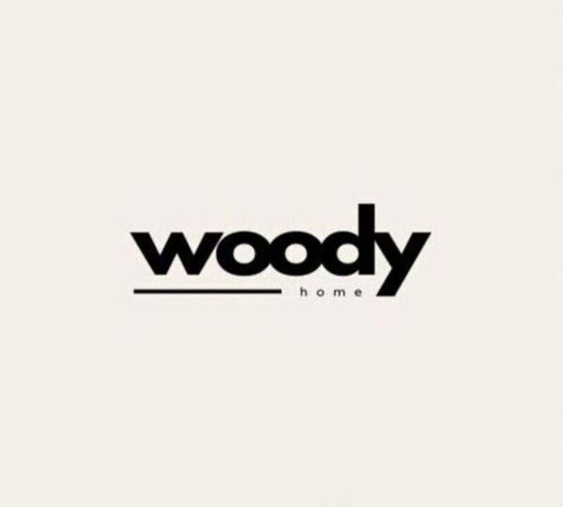 K&ouml;nnte beinhalten: Das Woody Home-Logo zeigt das Wort &bdquo;woody&ldquo; in fetter, schwarzer serifenloser Schrift, mit einem horizontalen Strich darunter. Unter dem Strich steht das Wort &bdquo;home&ldquo; in einer kleineren, d&uuml;nneren Schrift. Der Hintergrund ist hellcremefarben.