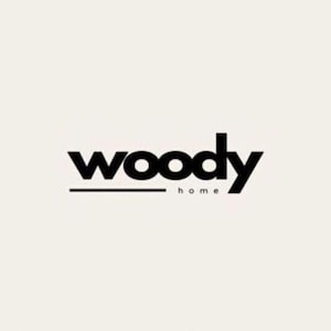 May include: The logo for "woody home" is displayed against a cream-colored background. The word "woody" is in bold, black, lowercase letters, with a thin black line beneath it. The word "home" is in smaller, black, lowercase letters below the line.