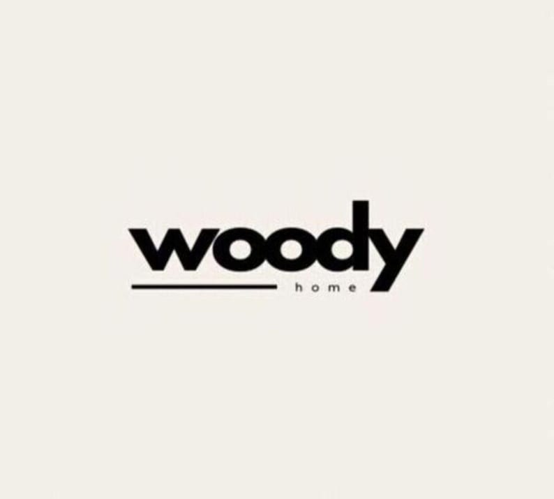 May include: The logo for "woody home" is displayed against a cream-colored background. The word "woody" is in bold, black, lowercase letters, with a thin black line beneath it. The word "home" is in smaller, black, lowercase letters below the line.