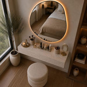 May include: A modern vanity setup with a large, irregularly shaped mirror with a warm, glowing border. The vanity features a light-colored countertop with makeup and brushes, a round stool, and a decorative rug. A potted plant adds a touch of nature.