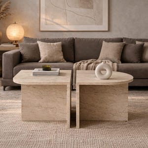 Peut inclure: Salon avec un canapé marron, des coussins et deux tables basses en pierre beige. Un tapis neutre et des objets décoratifs comme un vase et une lampe sont également présents. La pièce a une atmosphère chaleureuse et accueillante.
