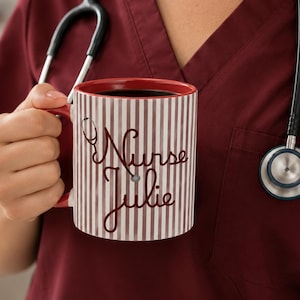 May include: A red and white striped coffee mug with the words "Nurse Julie" in a cursive font. The mug has a red interior and handle. A stethoscope hangs in the background.