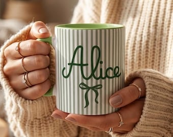 May include: A white ceramic mug with vertical green stripes and a green interior. The mug features the name "Alice" in green script with a bow design. The handle and the rim are green.