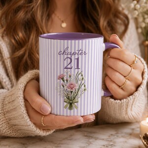May include: A ceramic mug with a light purple and white vertical striped pattern. The front features the text "chapter 21" in a dark purple script font above a detailed illustration of a floral bouquet with pink carnations and green foliage.