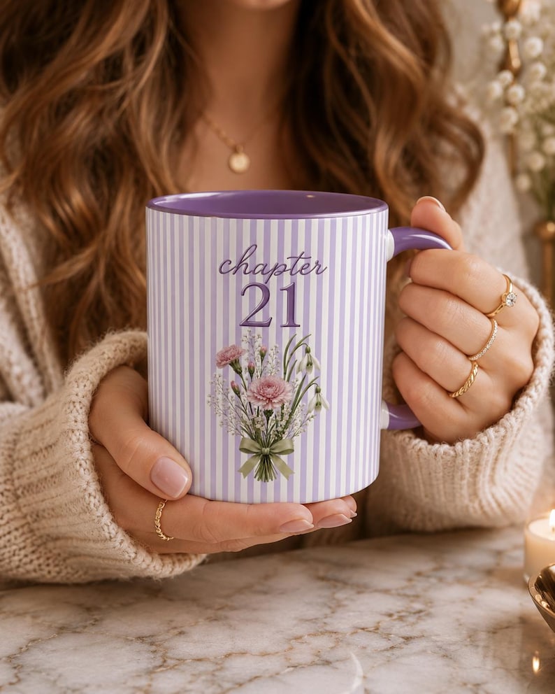 May include: A ceramic mug with a light purple and white vertical striped pattern. The front features the text "chapter 21" in a dark purple script font above a detailed illustration of a floral bouquet with pink carnations and green foliage.