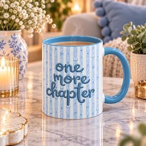 May include: A light blue and white striped ceramic mug with a blue handle and rim. The mug features the text one more chapter in raised dark blue lettering, surrounded by small blue icons of books, hearts, and bows on a vertical striped background.