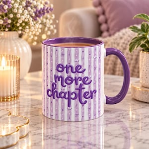 May include: A ceramic mug with a purple and white vertical striped pattern featuring the text one more chapter in bold purple lettering. The design includes small purple icons of books, bows, hearts, and stars scattered across the striped surface.