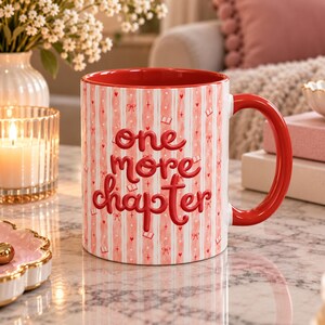 May include: A ceramic mug with a red interior and handle, featuring a white and light pink vertical striped pattern decorated with small red hearts, bows, and book icons. The text "one more chapter" is printed in a bold, raised red font.