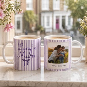 Peut inclure: Deux mugs en c&eacute;ramique blanche avec du caf&eacute;, pr&eacute;sentant un motif &agrave; rayures violettes. L'un des mugs porte l'inscription "Lucy's Mum" avec un n&oelig;ud, l'autre une photo et le texte "Mama's Little Love". Les mugs sont sur un rebord de fen&ecirc;tre.