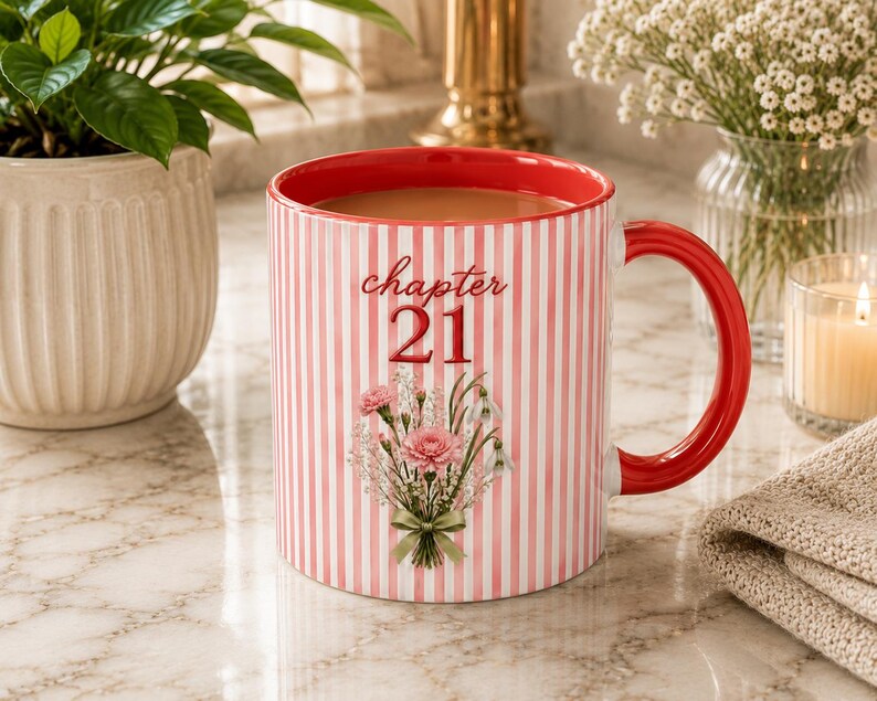 May include: A ceramic mug with a red and white vertical striped pattern, featuring the text 'chapter 21' in red script above a printed bouquet of pink carnations and white flowers. The mug has a solid red interior and a matching red handle.