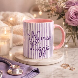 May include: A ceramic mug with a pink interior and handle, featuring vertical purple and white stripes. The mug is inscribed with the words "Nurse Lizzie" in purple script, along with a stethoscope graphic.