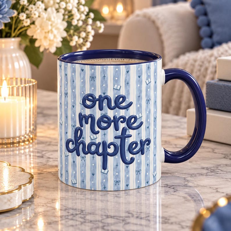 May include: A ceramic mug with a dark blue interior and handle, featuring a light blue and white vertical striped pattern. The mug displays the dark blue text "one more chapter" in a rounded font, accented by small book and bow icons.