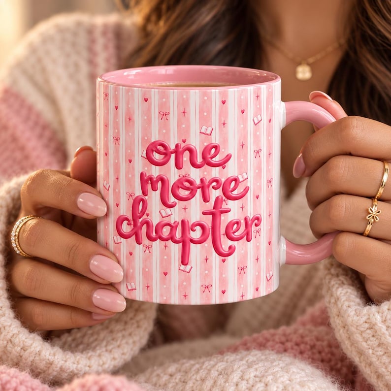 May include: A pink ceramic mug featuring vertical white stripes and the text one more chapter in bold pink lettering. The surface is decorated with small pink hearts, bows, and open book icons. The mug has a matching pink handle and a smooth finish.