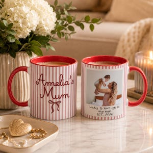 Peut inclure: Deux mugs en c&eacute;ramique avec des anses et des bords rouges. L'un des mugs porte l'inscription "Amelia's Mum" en &eacute;criture cursive avec un n&oelig;ud. L'autre mug pr&eacute;sente une photo d'une m&egrave;re et d'un enfant avec le texte "Lucky to have you as my mum EST. 2026". Les deux mugs ont un motif &agrave; rayures.