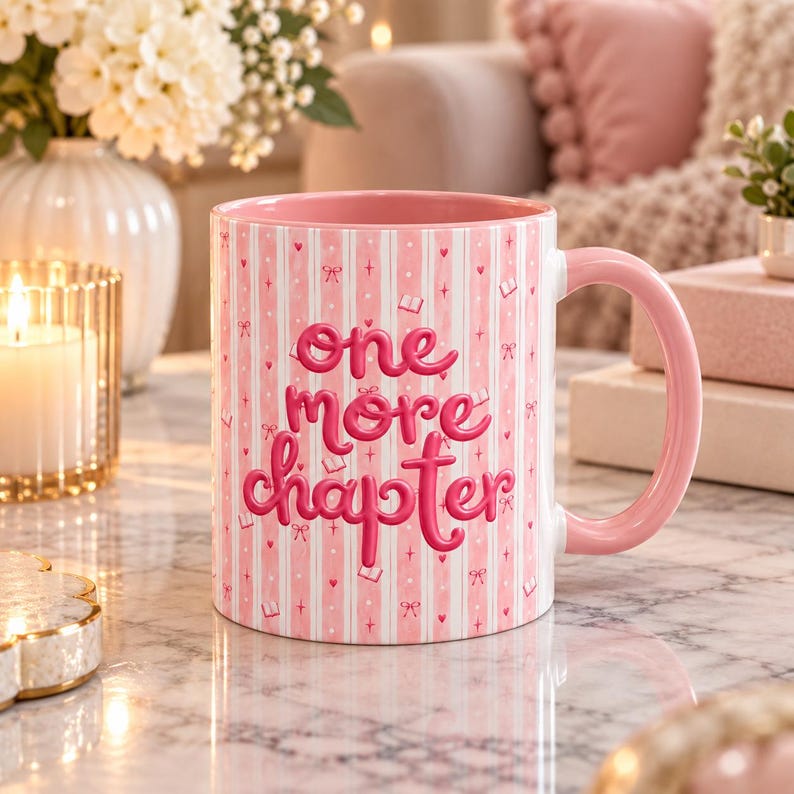 May include: A ceramic mug with a pink and white vertical striped pattern, featuring the text "one more chapter" in bold pink script. The mug has a solid pink interior and a matching pink handle, decorated with small pink hearts and book icons.