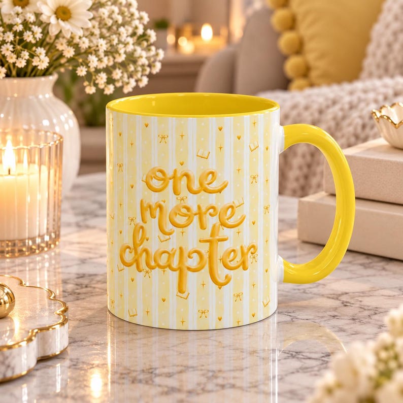 May include: A yellow ceramic mug with a bright yellow interior and handle. The exterior features a light yellow and white vertical striped pattern with small gold icons and the embossed text "one more chapter" in a rounded yellow font.