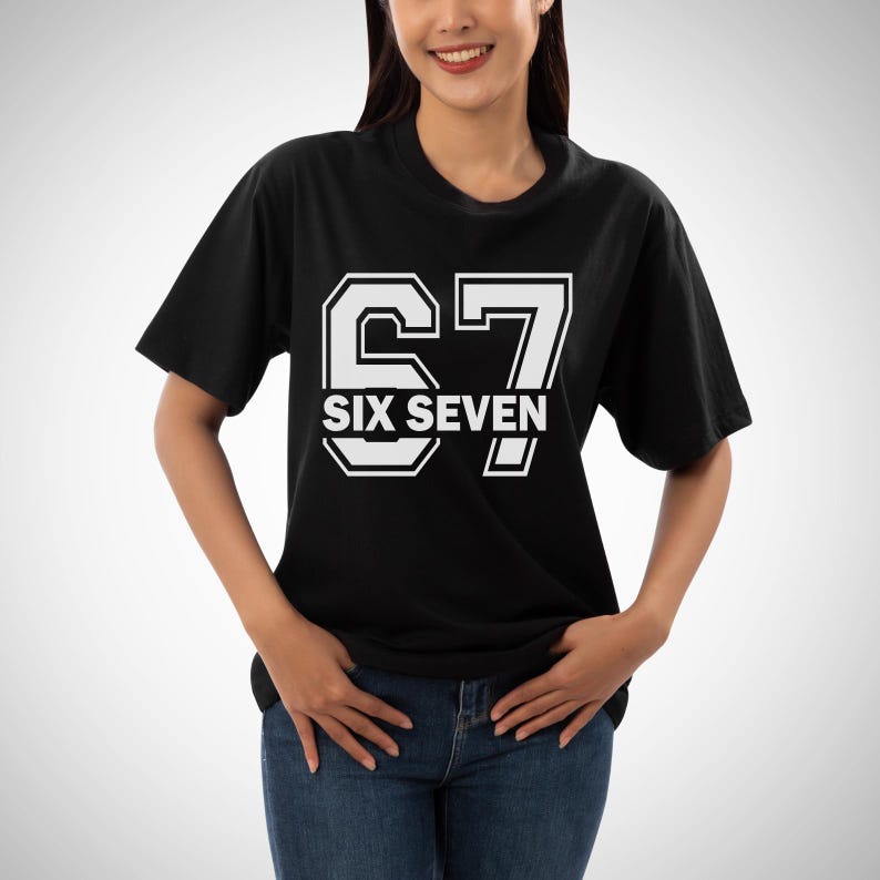 May include: Black t-shirt with the number "67" and the words "SIX SEVEN" in white, outlined in a collegiate style. The shirt is a classic crew neck design.
